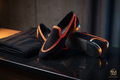 Lifestyle concept presentation of black women's slip-on shoes with orange geometric edging and gold-tone heel accents.