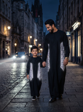 Father and son holding hands on a cobbled street at dusk, wearing matching black thobes with bright silver-white geometric side panels.