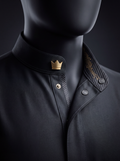 Close-up of a matte black thobe collar on a mannequin, with a gold-tone crown insignia, grey press studs and gold circuit-inspired detailing on carbon-pattern trim.