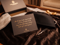Concept unboxing presentation with Arabic welcome card, black patterned cap, silver-tone horn-shaped pendant and open Casa Massafra gift packaging.